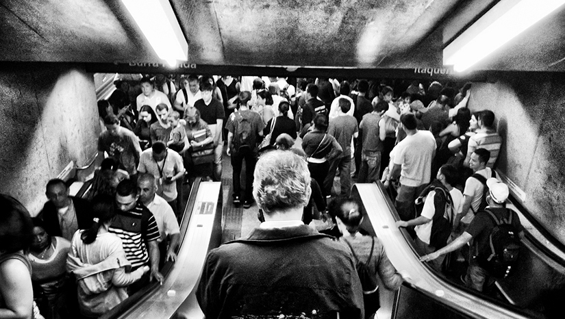 A photo of a crowded subway station full of people going up and down escalators
