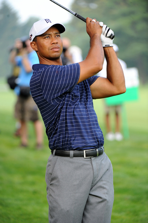 A photo of golfer Tiger Woods holding his golf club up in the air on the golf course after hitting a golf ball