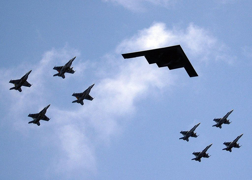 A formation of airplanes featuring fighter jets and a stealth bomber is shown in the sky.