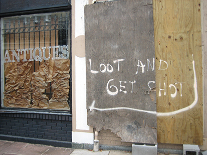 A photo of a damaged home from Hurricane Katrina with a sign posted on the fence that reads, Looters Will Be Shot