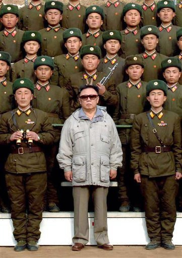 Kim Jong-Il of North Korea is shown wearing sunglasses amid a group of uniformed North Korean soldiers.