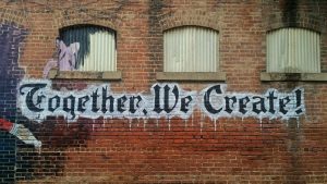 "Together, We Create" written in graffiti on a brick wall