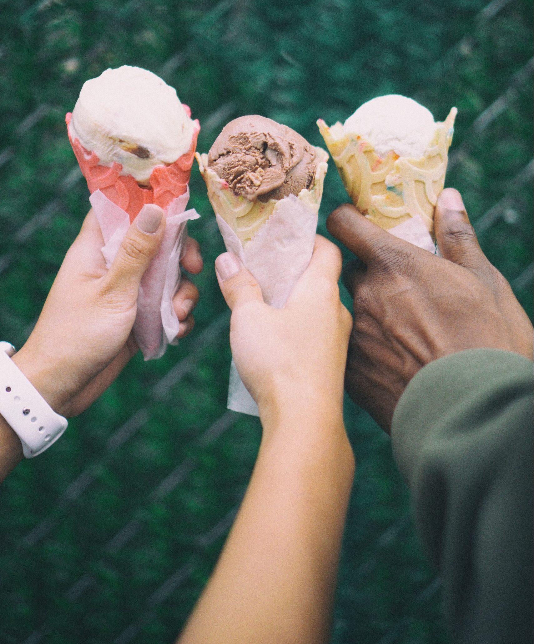 The hands of 3 friends, each holding an ice cream cone.