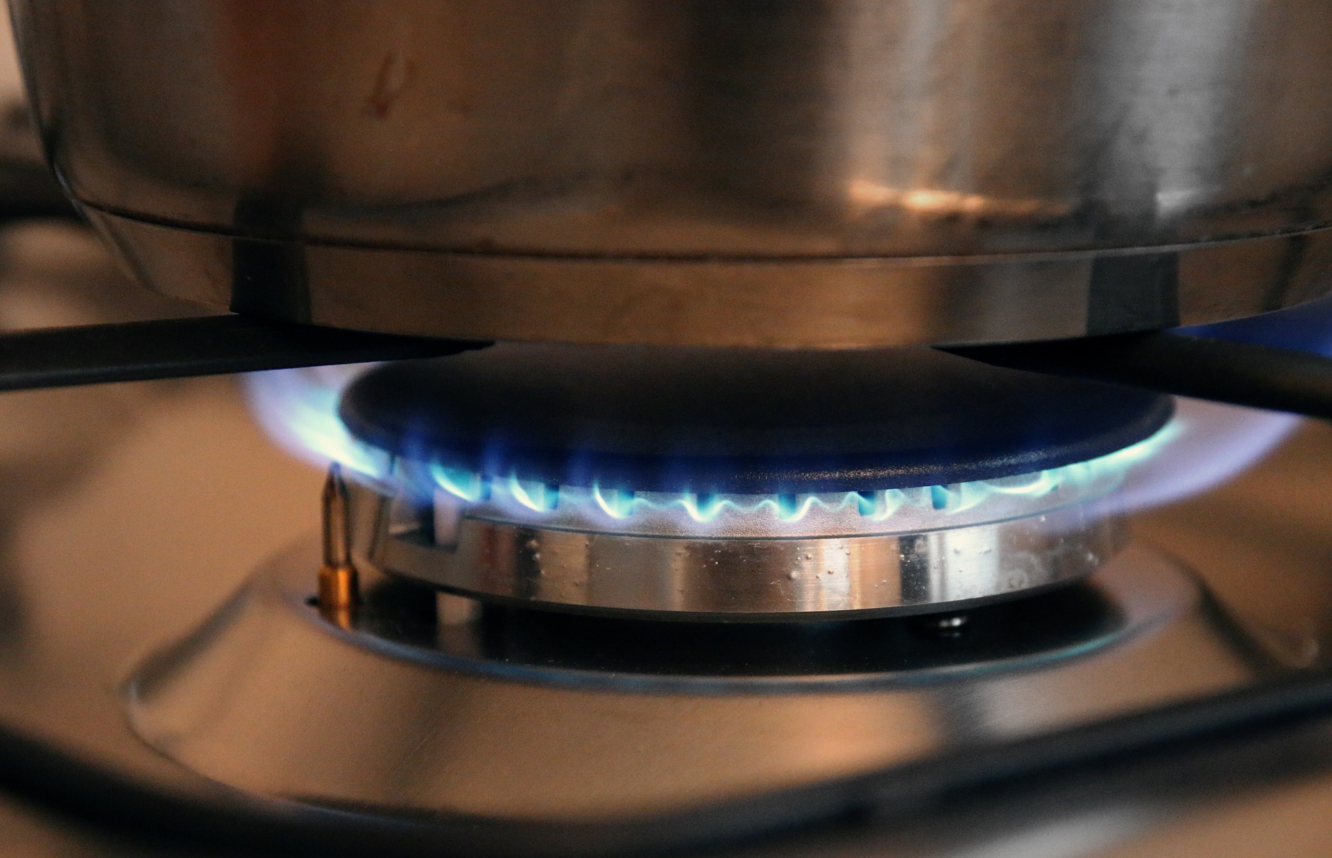 Image shows a lit gas stove burner. The flames are blue and there is a pot on the burner.