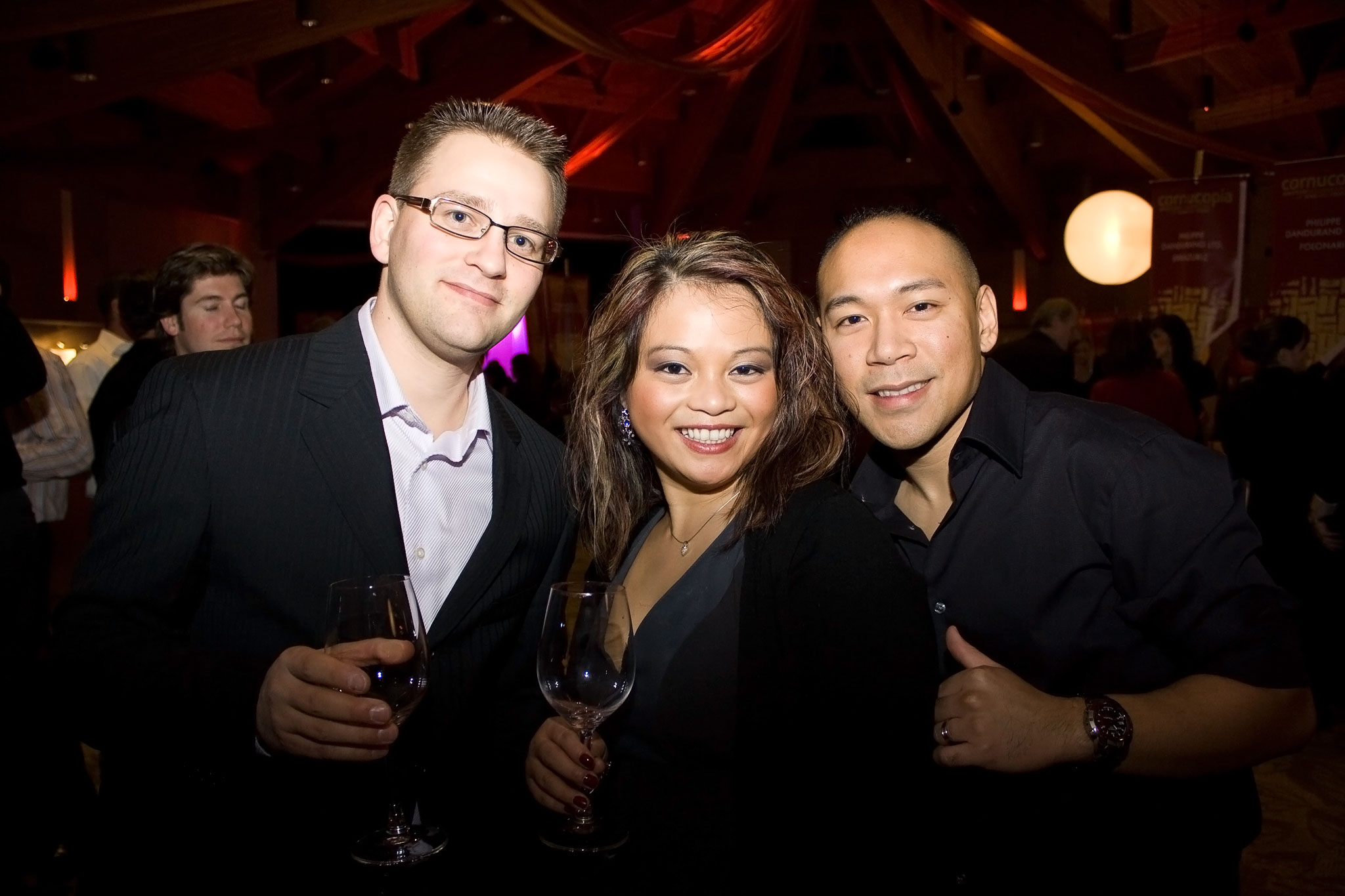 Three people in semi-formal clothes hold wine glasses at a festival.