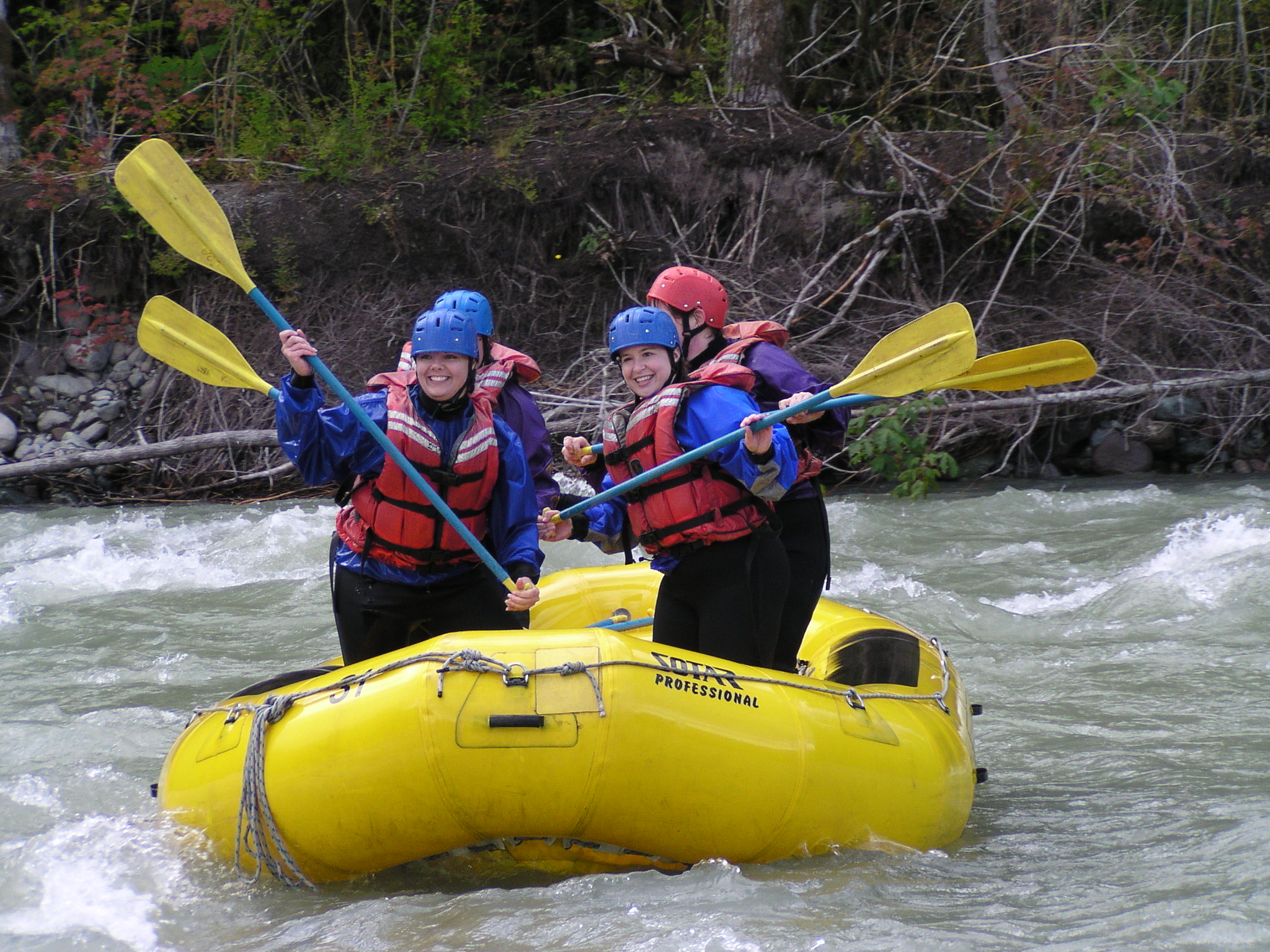 Rafters pose with their paddles, standing in a raft on a river.