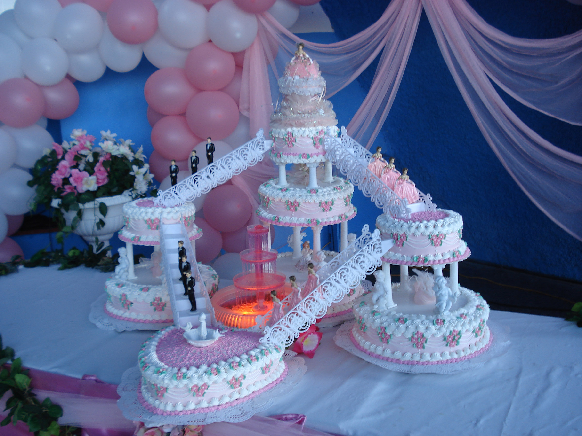 An elaborate multi-tiered pink cake that has both male and female figures along the sides, but a single lavishly-dressed figure at the top.