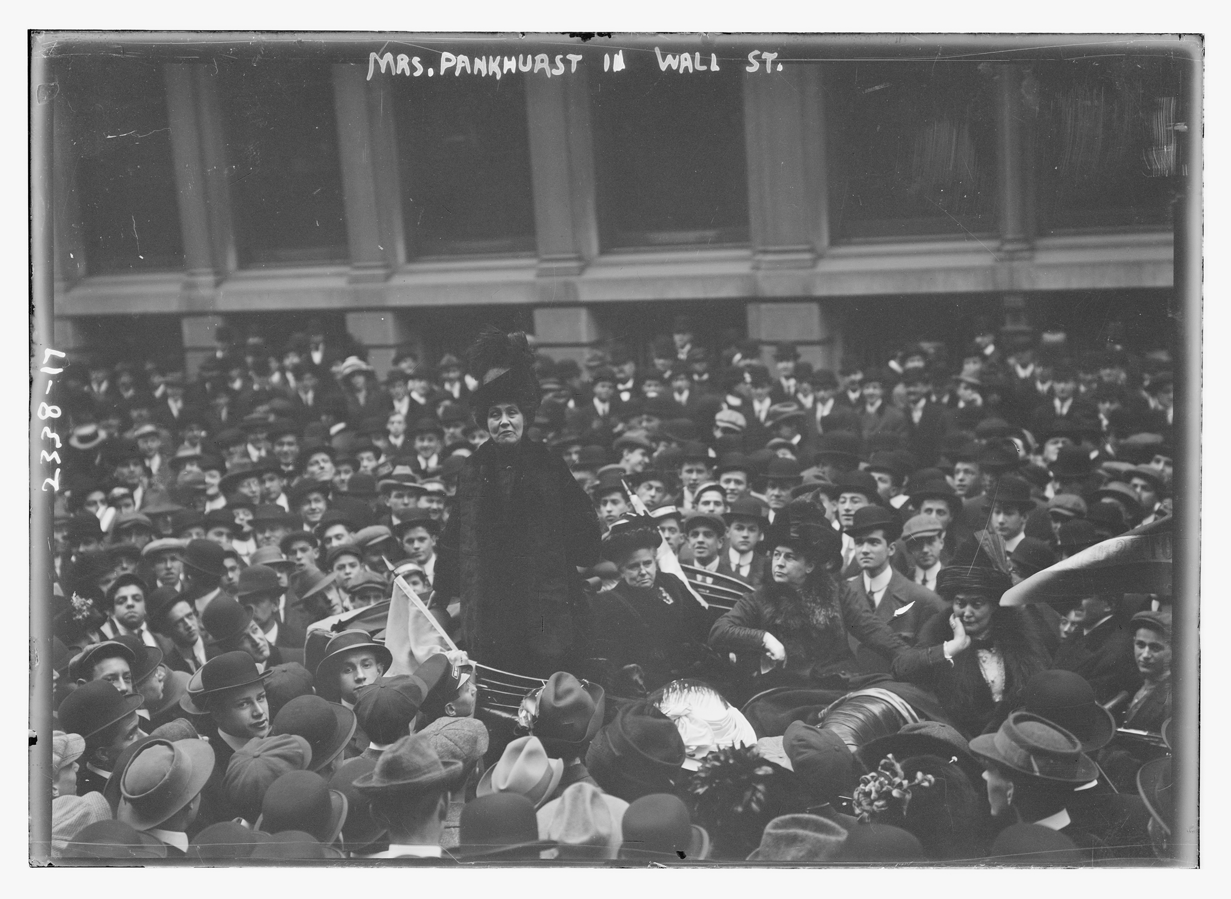 A black-and-white photo of a woman in dark clothing standing up in a car surrounded by a large crowd.