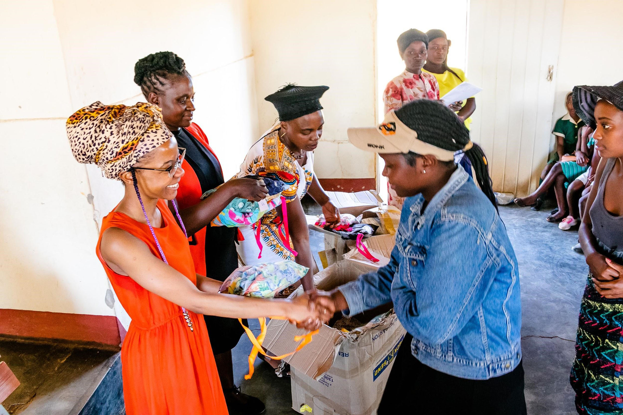 Two African woman shaking hands, distributing a bag of washable sanitary ware.