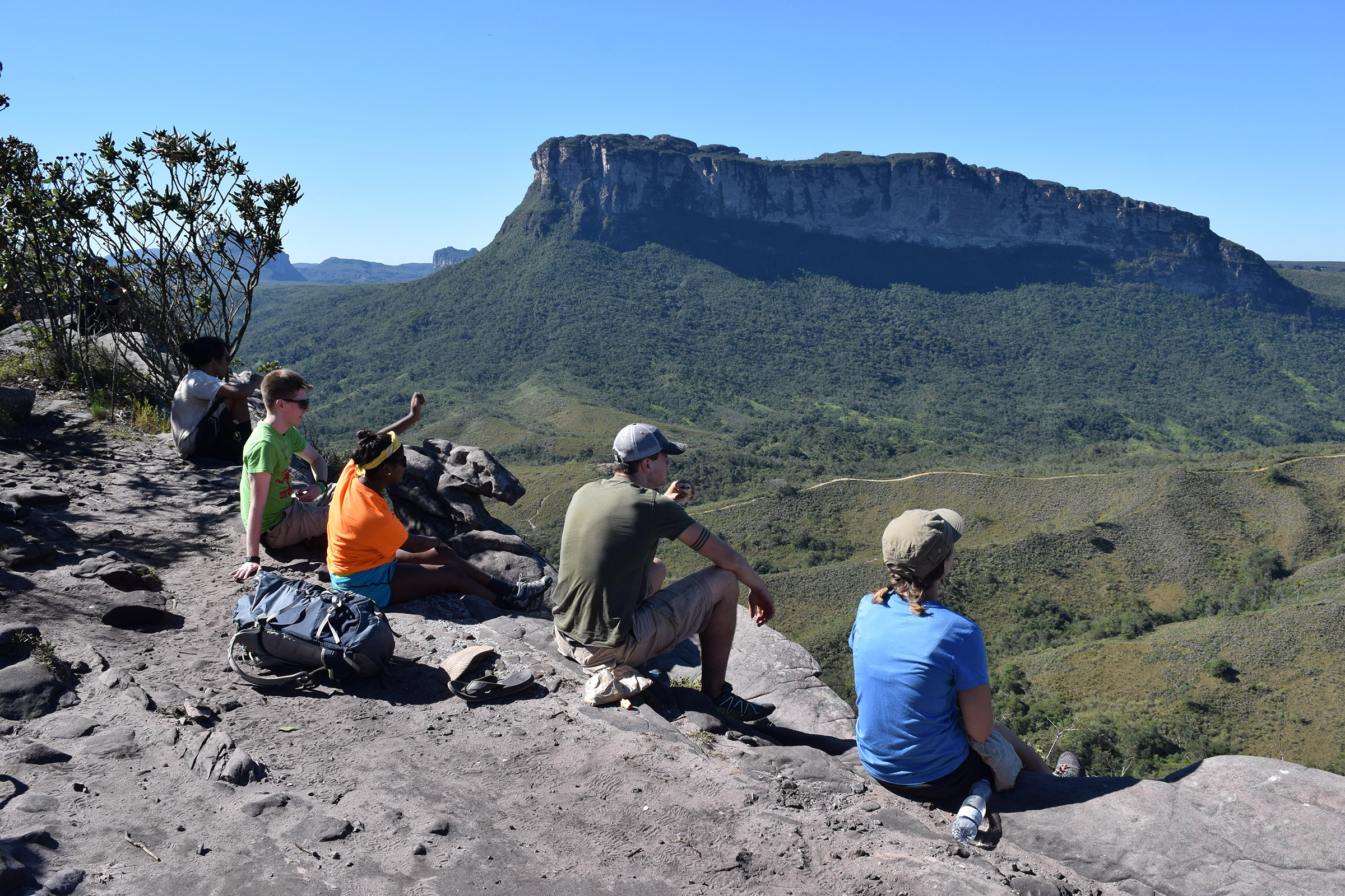 Five students sit on a ledge overlooking a large, elongated rock-faced mountain.