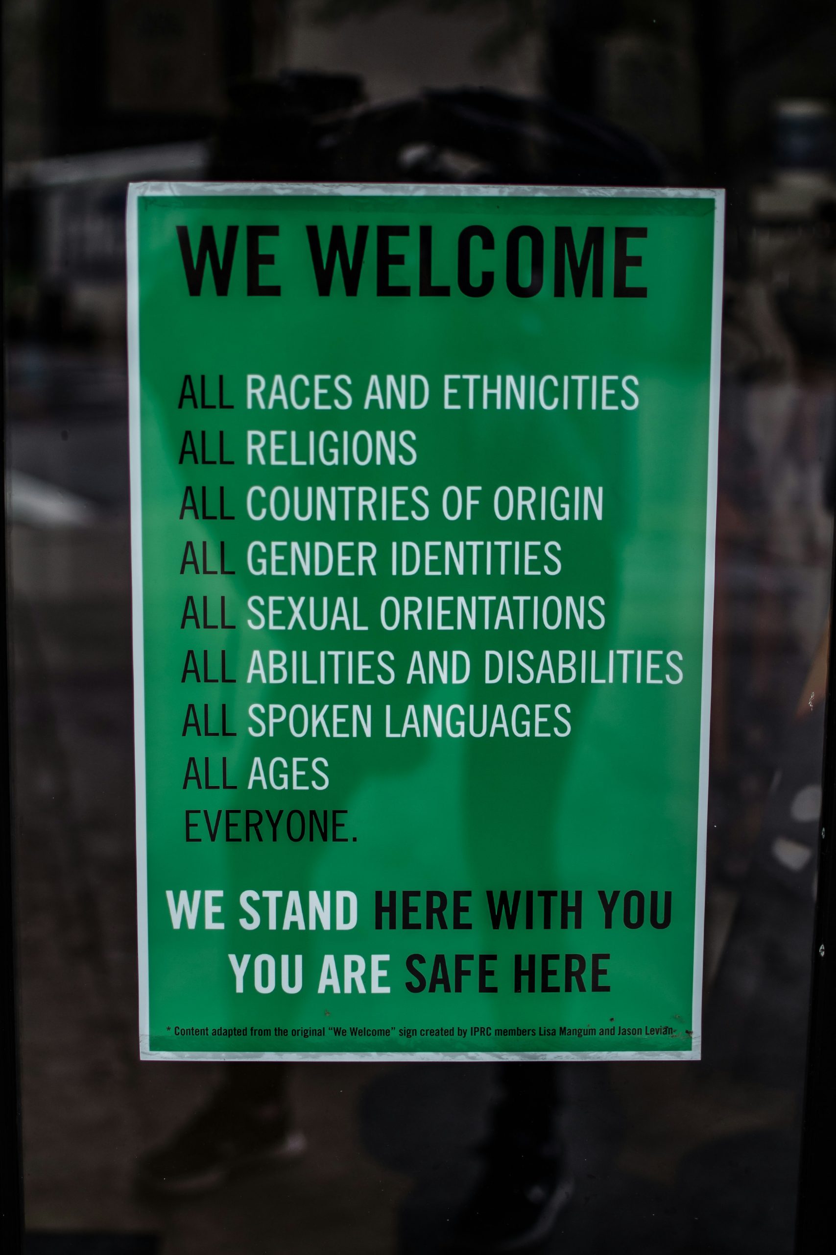 A green sign in a window reads, “We welcome all races and ethnicities; all religions; all countries of origin; all gender identities; all sexual orientations; all abilities and disabilities; all spoken languages; all ages. Everyone. We stand here with you. You are safe here.”