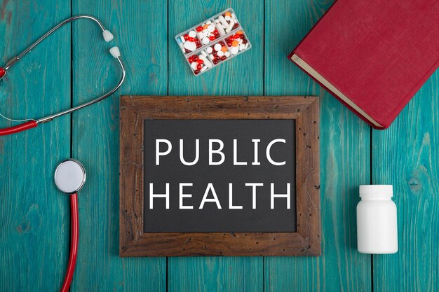 A graphic showing the words "public health" along with a red book, a red and white stethoscope, a white pill bottle and a pill box with different color pills.