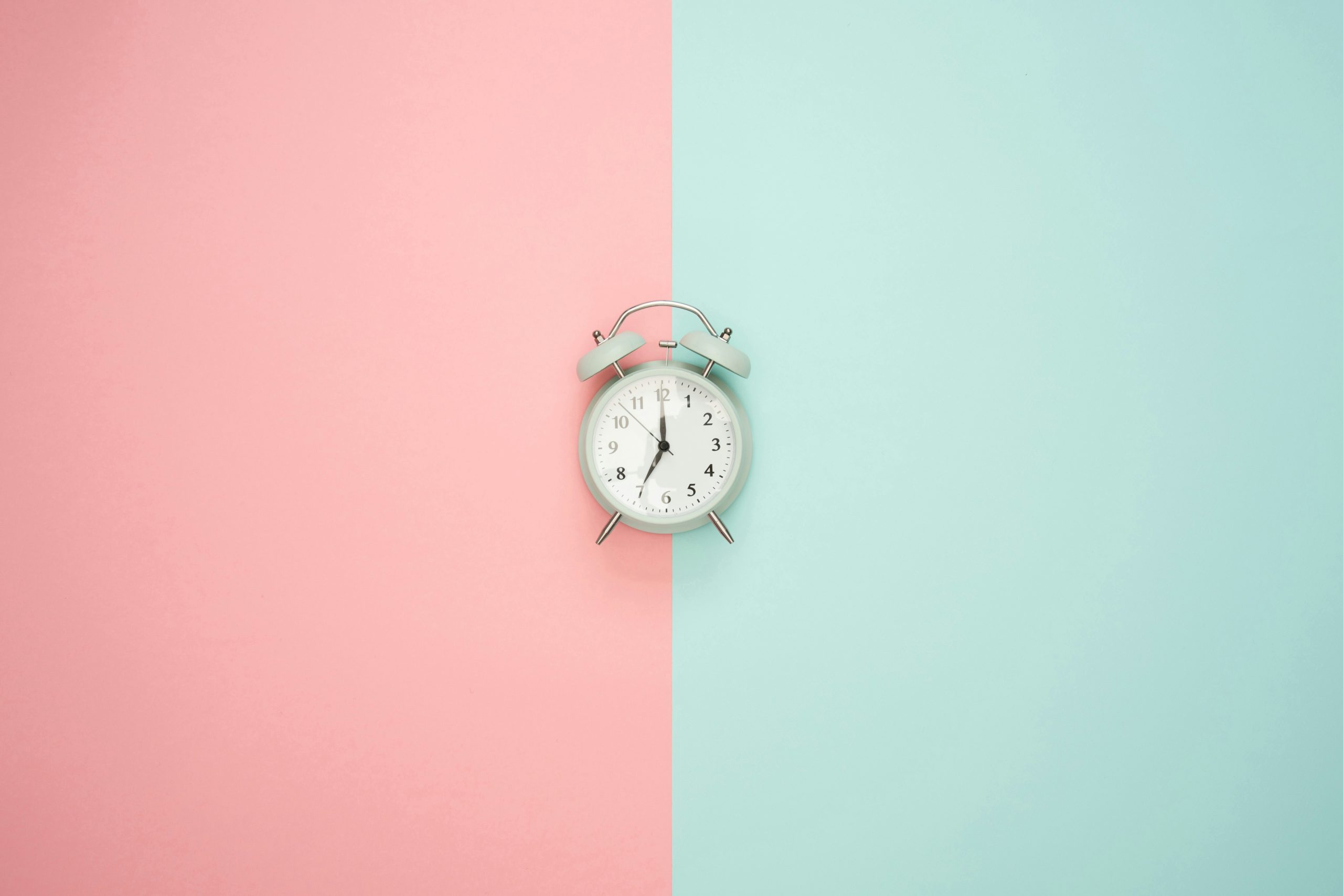 A clock pictured in front of a colored background split in half: blue on the right, pink on the left.