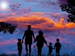 Image of a man, woman, and 3 children holding hands, silhouetted against a sunset with birds flying in the distance.