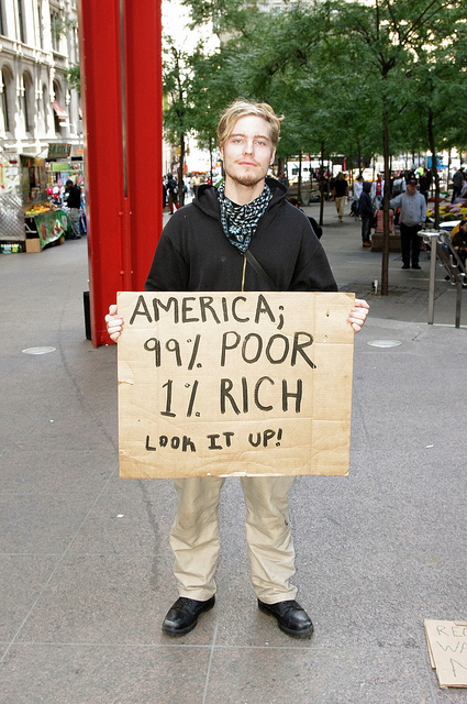Photo of a young man holding a protest sign, which reads: "America: 99% Poor, 1% Rich. Look it up!"