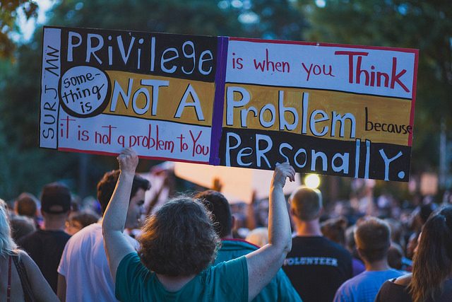 A protest sign reads: "Privilege is when you think something is not a problem because it is not a problem to you personally.