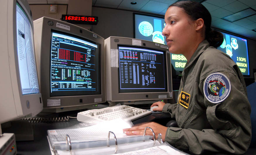 Photograph of a space systems operator using several computer monitors showing various data.